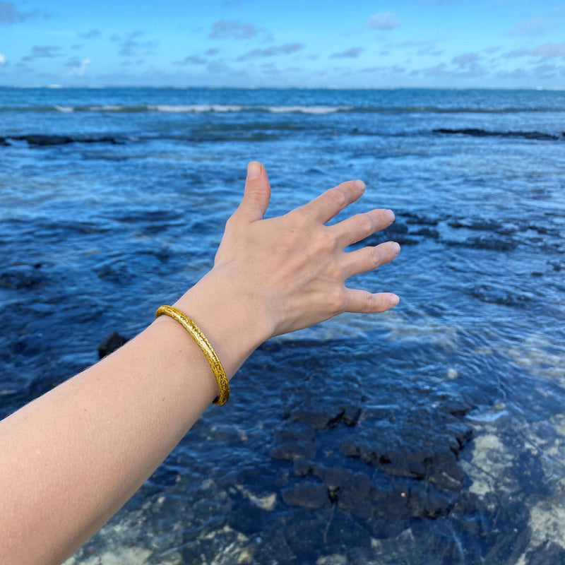 The Forged by the Ocean ladies Gold Cuff Bangle on model image with an ocean view.